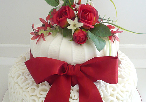 A wedding cake with big red bow and flowers